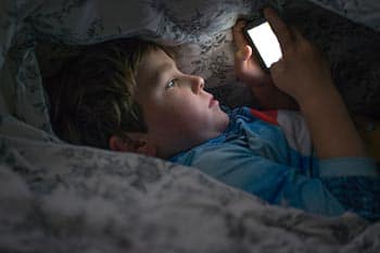 Young boy on cell phone under duvet